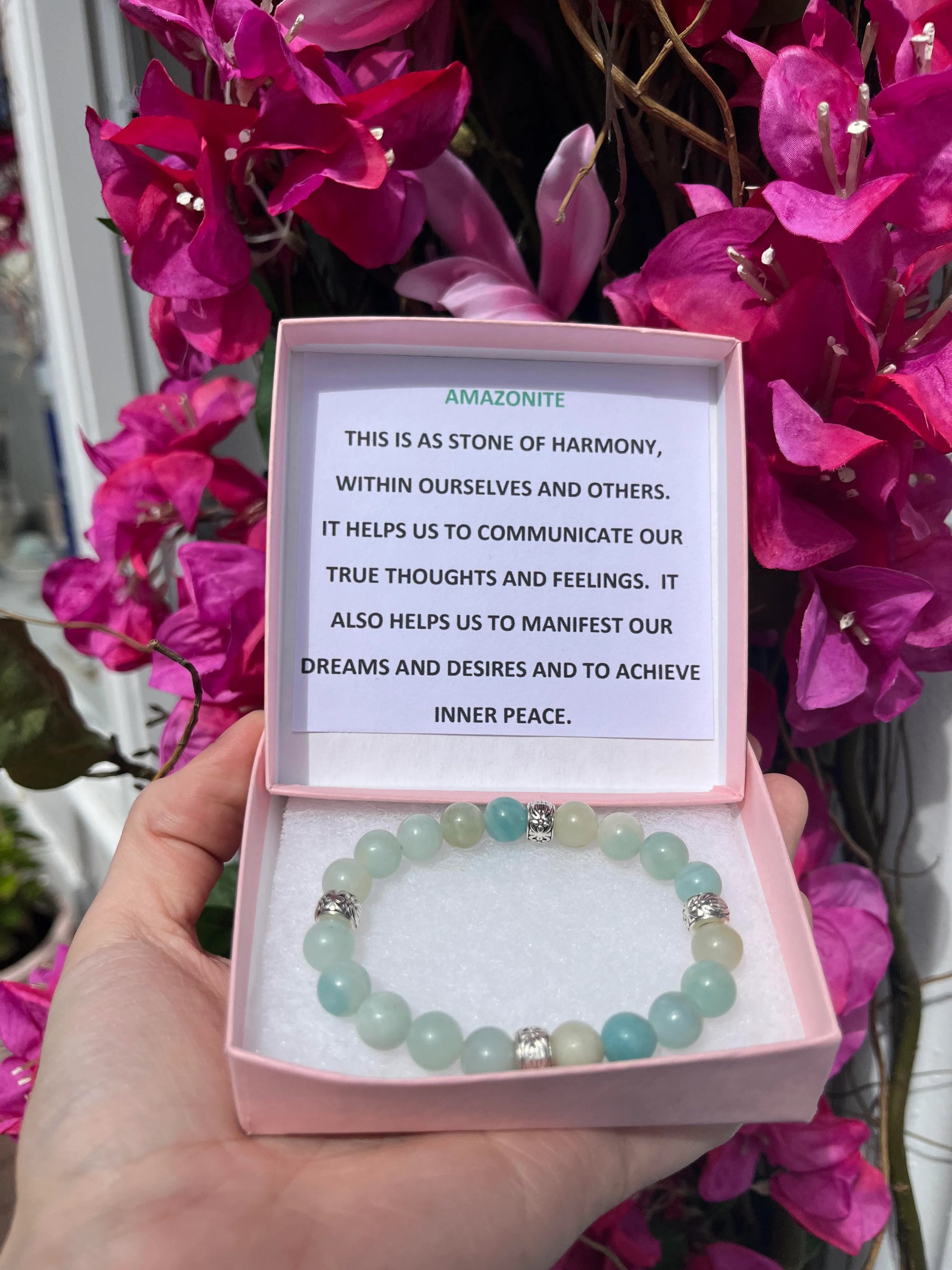 A crystal bracelet in a pink box with a typed description in the lid that reads - Amazonite - This is a stone of harmony, within ourselves and others. It helps us to communicate our true thoughts and feelings. It also helps us to manifest our dreams and desires and to achieve inner peace.