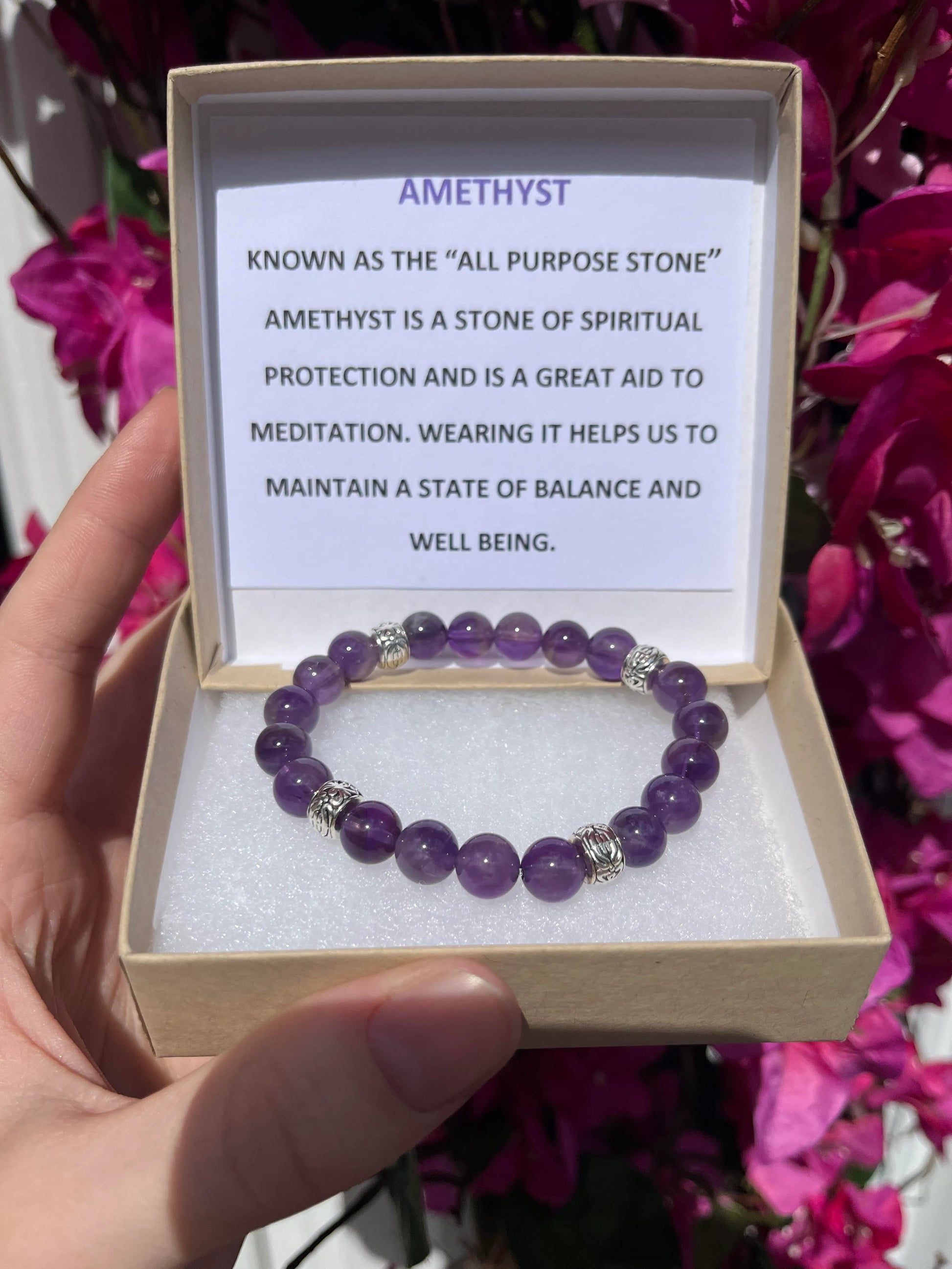 A crystal bracelet in a brown box with a typed description in the lid that reads - Amethyst: Known as the "all purpose stone" amethyst is a stone of spiritual protection and is a great aid to meditiation. Wearing it helps us to maintain a state of balance and wellbeing.
